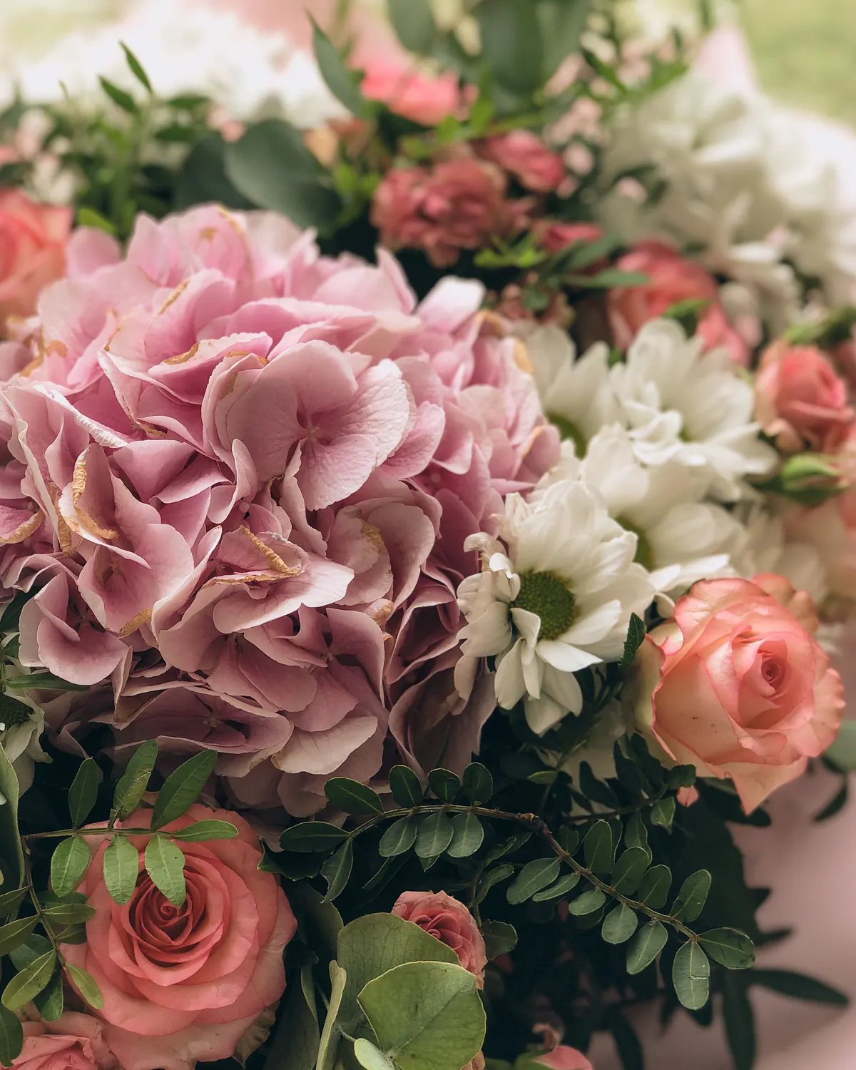 A medium bouquet of pink hydrangea, coral roses and white daisies in pink paper.